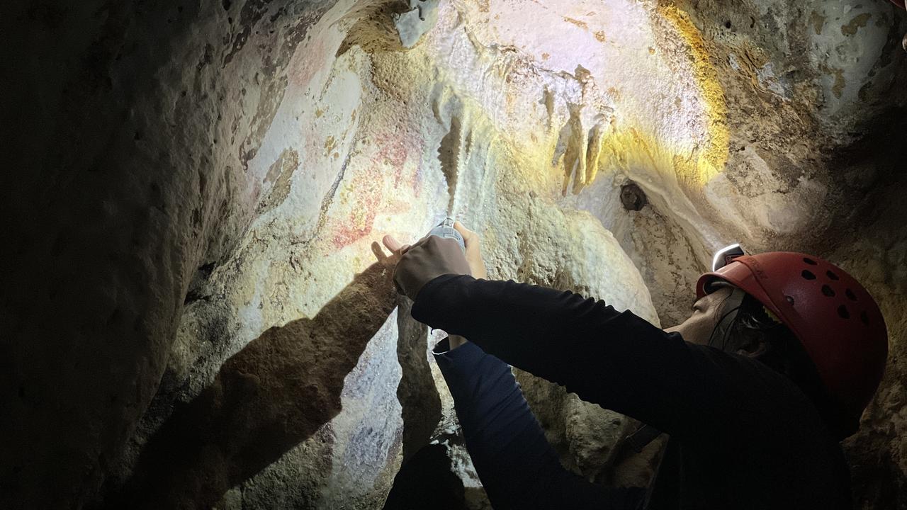 Ein Mensch zeigt in einer Höhle eine Höhlenmalerei.