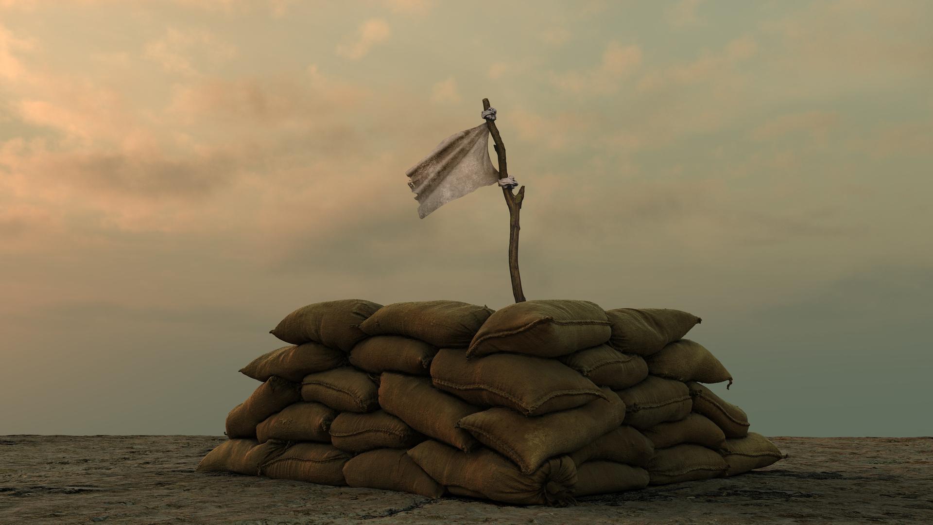 Eine weisse Flagge an einem Stock hinter einer militärischen Sandsackbarrikade vor einem trüben Himmel.