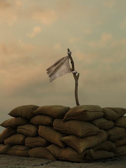 Eine weisse Flagge an einem Stock hinter einer militärischen Sandsackbarrikade vor einem trüben Himmel.