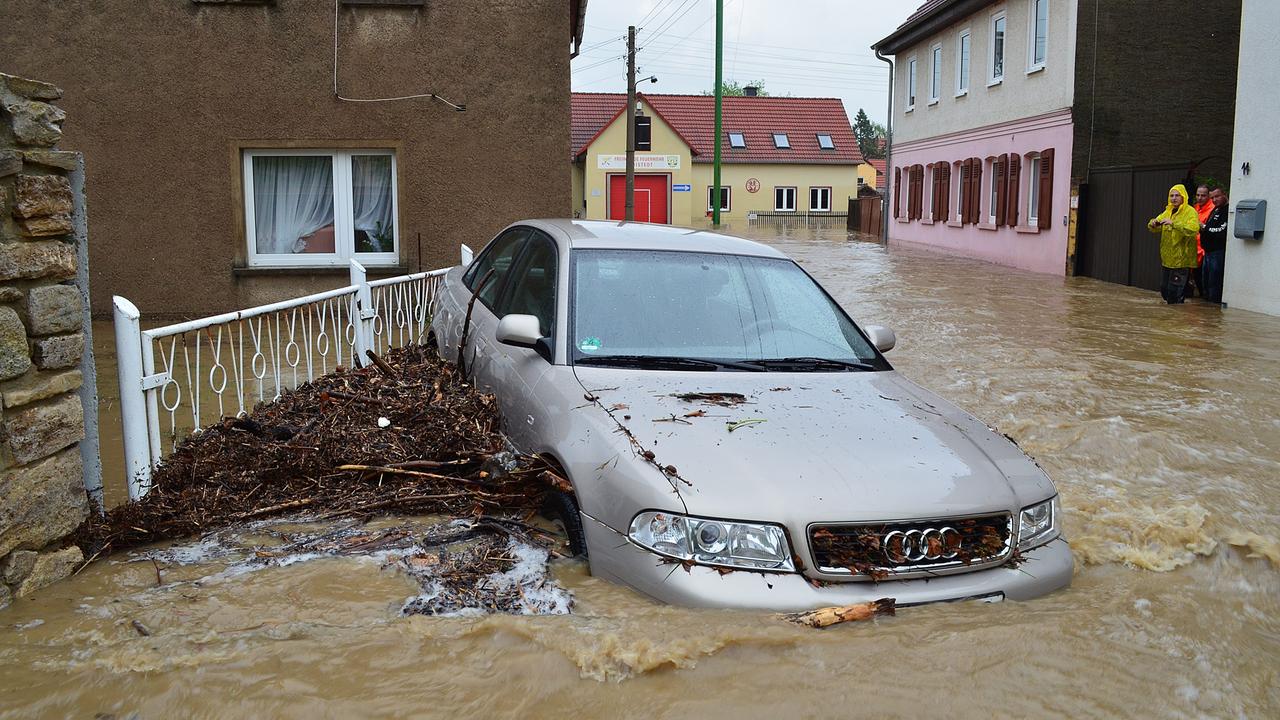 Ein Auto wird von einer Flut durch eine überschwemmte Straße getragen. 