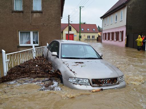 Ein Auto wird von einer Flut durch eine überschwemmte Straße getragen. 