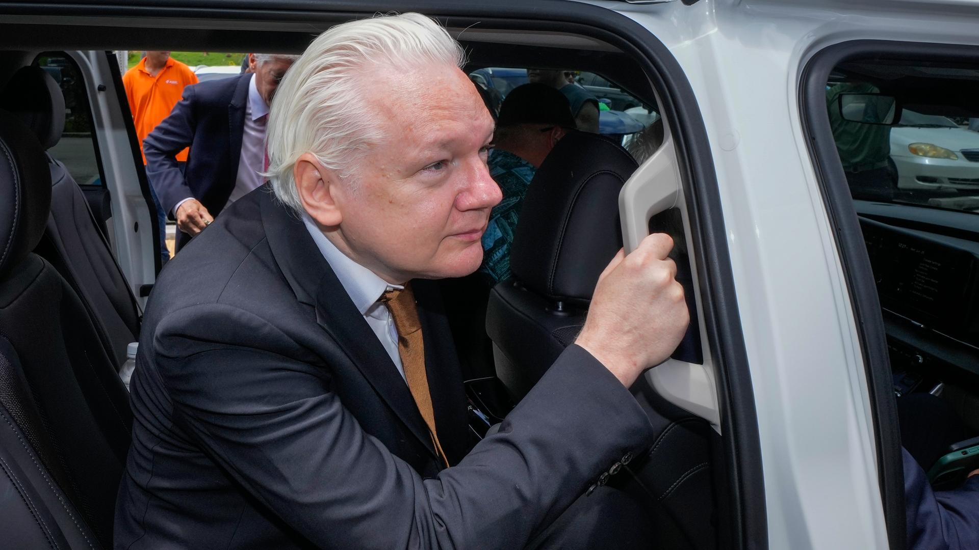 Assange im schwarzen Anzug steigt in das weiße Auto und hält sich dabei an einem Griff fest. Assange im schwarzen Anzug steigt in das weiße Auto und hält sich dabei an einem Griff fest.