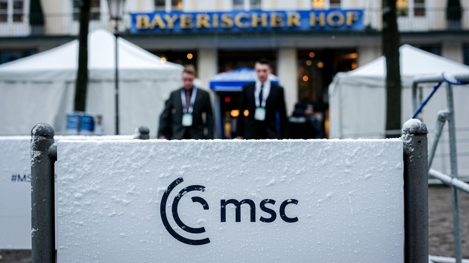 Schnee liegt am Abschlusstag der 62. Münchner Sicherheitskonferenz (MSC) vor dem Hotel Bayrischer Hof auf einem Schild. Im Hintergrund sieht man in der Unschärfe den Eingangsbereich des Hotels.