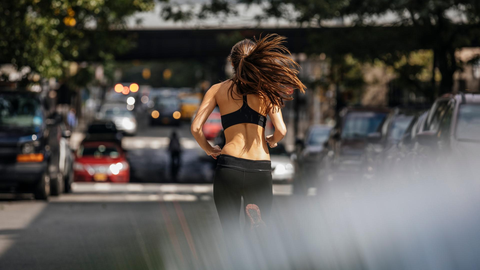 Eine junge Frau ist beim Joggen in einer Stadt von hinten zu sehen