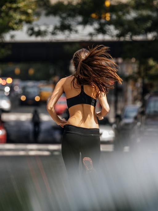 Eine junge Frau ist beim Joggen in einer Stadt von hinten zu sehen