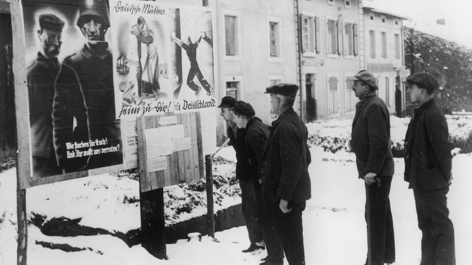 Historisches Schwarzweißfoto von Männern, die sich Propagandaplakate für ein deutsches Saarland anschauen.