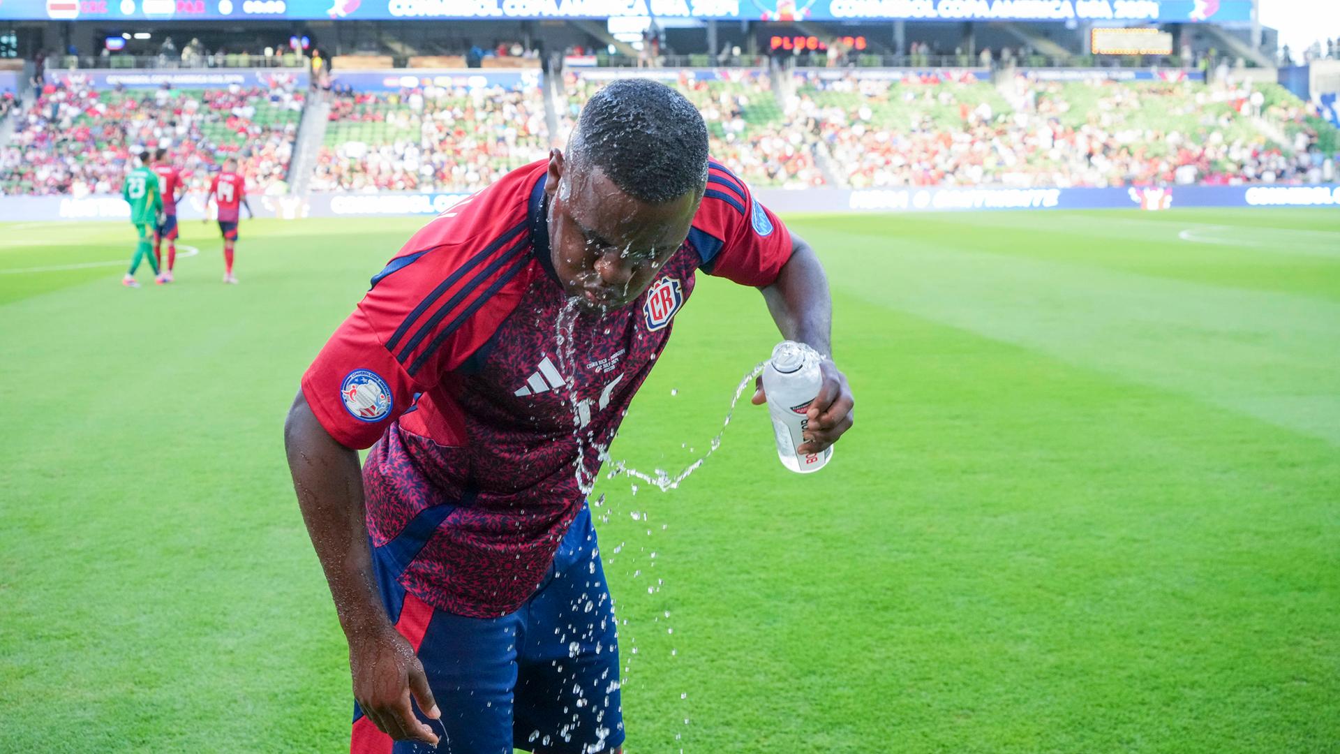 Ein Fußballspieler schüttet sich Wasser über den Kopf.