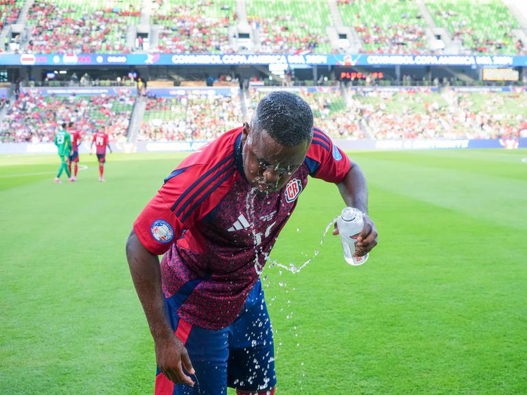 Ein Fußballspieler schüttet sich Wasser über den Kopf.