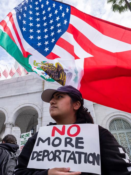 Zwei Demonstrantinnen gegen die Migrationspolitik von Trump in Los Angeles. Eine Frau schwenkt eine US-Fahne, eine trägt ein Schild mit den Worten "No more deportations" (Keine Deportationen mehr) 