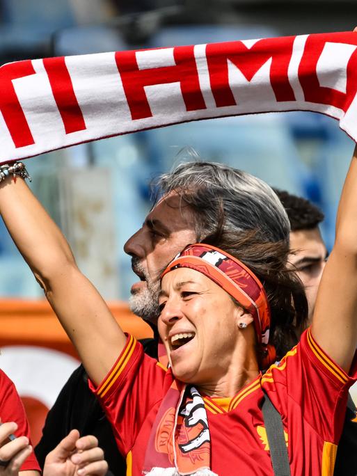 Eine Frau hält einen Schal in die Höhe, auf dem "Ti amo" steht, was auf Italienisch "Ich liebe Dich" bedeutet. Sie schaut glücklich. 