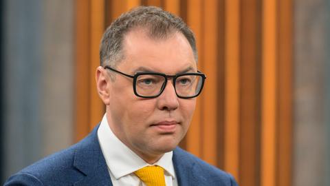 Oleksij Makejew, Botschafter der Ukraine in Deutschland, bei einem Besuch der Talkshow von Caren Miosga. Er trägt einen Anzug und eine dunkle Brille, im Hintergrund ist orange-brauner Stoff zu sehen. 