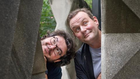 Devid Striesow und Axel Ranisch stehen zwischen Formbausteinen aus der DDR und schauen amüsiert in die Luft. Devid Striesow und Axel Ranisch stehen zwischen Formbausteinen aus der DDR und schauen amüsiert in die Luft.