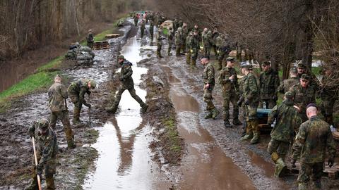 Soldatinnen und Soldaten der Bundeswehr sichern einen Deich an der Helme mit Sandsäcken.