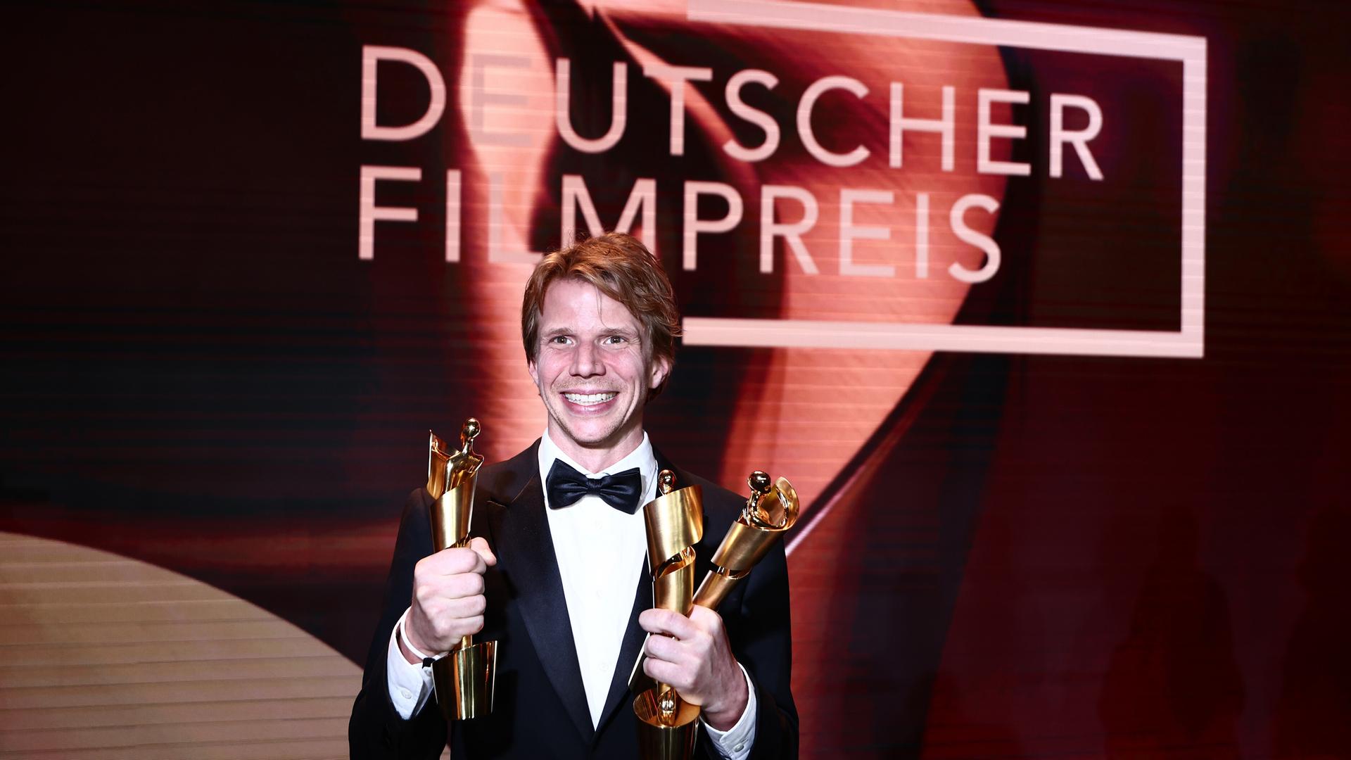 Regisseur Tim Fehlbaum hält drei der neun Lolas für den Film "September 5" während der 75. Verleihung des Deutschen Filmpreises in Berlin im Theater am Potsdamer Platz. Er strahlt.