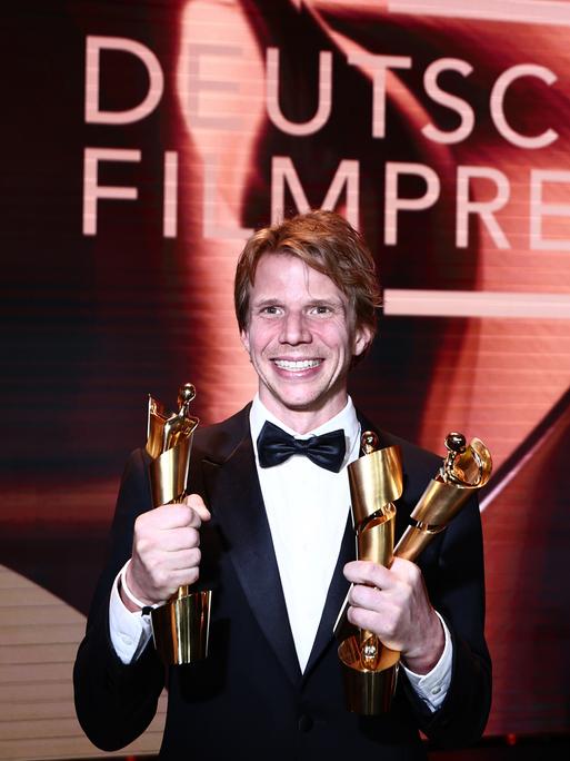Regisseur Tim Fehlbaum hält drei der neun Lolas für den Film "September 5" während der 75. Verleihung des Deutschen Filmpreises in Berlin im Theater am Potsdamer Platz. Er strahlt.