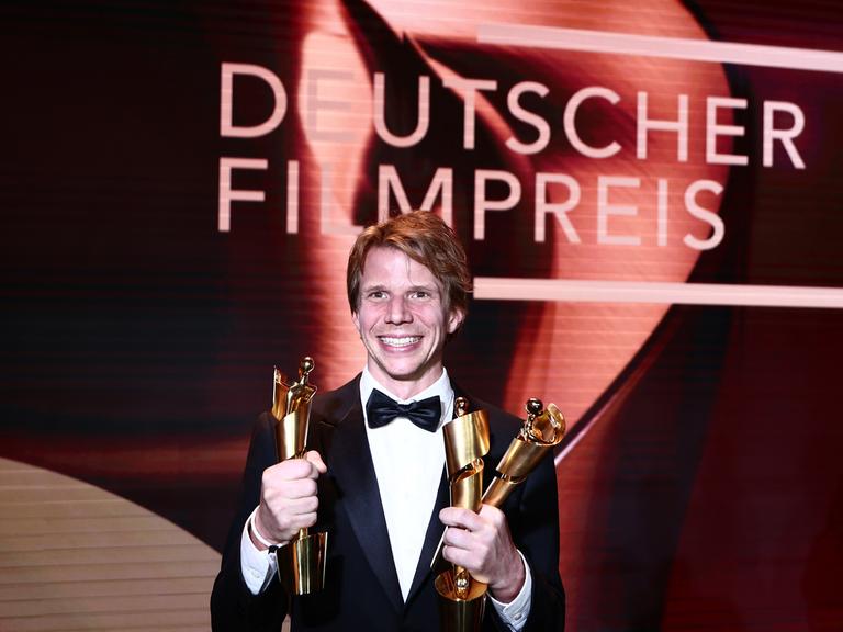 Regisseur Tim Fehlbaum hält drei der neun Lolas für den Film "September 5" während der 75. Verleihung des Deutschen Filmpreises in Berlin im Theater am Potsdamer Platz. Er strahlt.