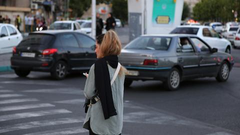 Eine junge Frau läuft in Teheran ohne den vorgeschriebenen Kopfschleier auf der Straße zwischen Autos.