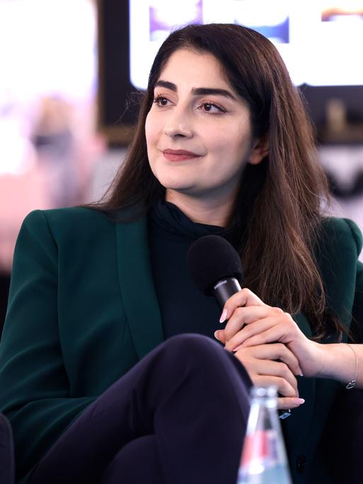 Waslat Hasrat-Nazimi sitzt bei einem Gespräch auf der Frankfurter Buchmesse 2022 mit einem Mikrofon in der Hand in einem Sessel.