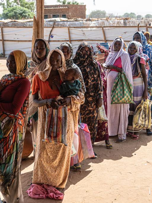 Sudanesische Fraeun und Kinder warten in einer Registrierungsstelle in Adre, Tschad, in einer Schlange auf die Verteilung von Hilfsgütern 