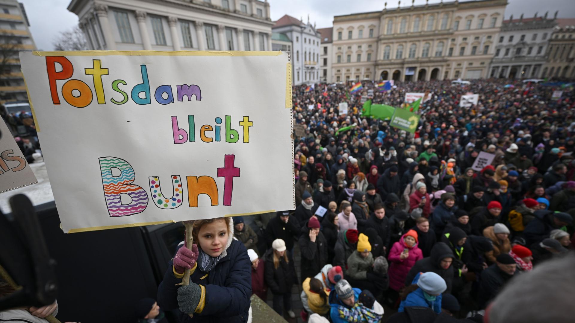 Eine Menschenmenge hat sich auf einem Platz versammelt. Ein Mädchen hält ein Schild in die Höhe. Darauf steht "Potsdam bleibt Bunt".