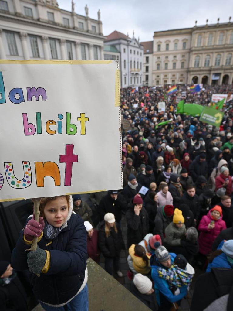 Eine Menschenmenge hat sich auf einem Platz versammelt. Ein Mädchen hält ein Schild in die Höhe. Darauf steht "Potsdam bleibt Bunt". 