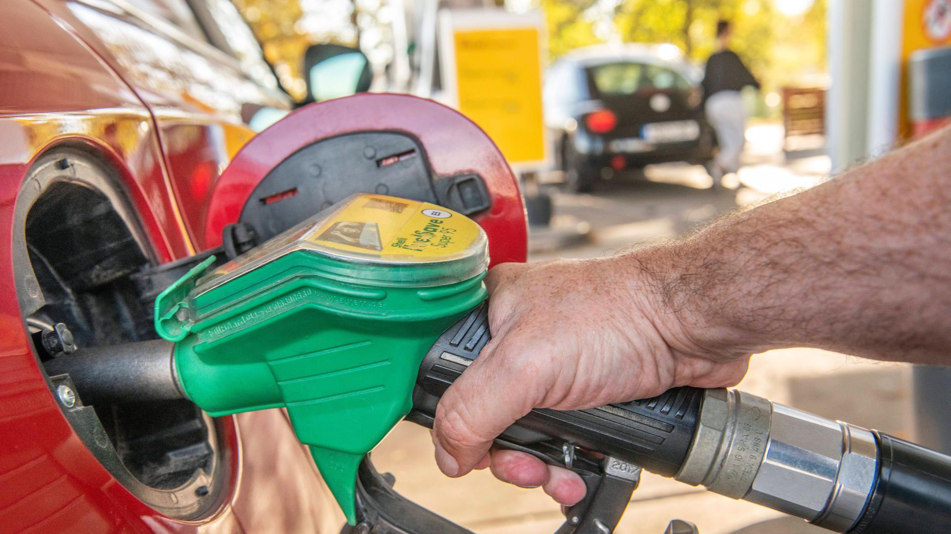 Eine Hand hält den Zapfhahn in sein Auto an einer Tankstelle. 