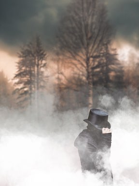 Professor van Dusen: Ein Mann mit unkenntlichem Gesicht im Mantel, der mit seiner Hand an seinen Zylinder fasst. Er steht im Nebel vor einem düsteren winterlichen Wald Professor van Dusen: Ein Mann mit unkenntlichem Gesicht im Mantel, der mit seiner Hand an seinen Zylinder fasst. Er steht im Nebel vor einem düsteren winterlichen Wald