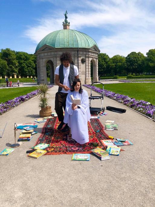 Ein Friseur schneidet einer Frau in einem Park die dunklen Haare. Sie liest dabei in einem Buch.