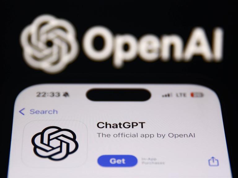 Ein Smartphone mit geöffneter ChatGPT-App und im Hintergund das Logo des Unternehmens OpenAI