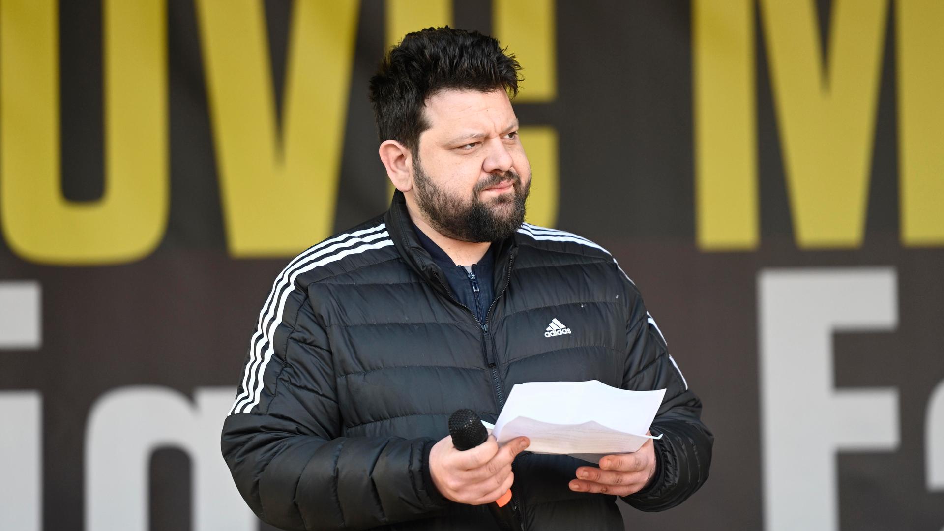 Petar Rosandic spricht auf einer Kundgebung, hält ein Redemanuskript und Mikrofon in den Händen und blickt zur Seite.