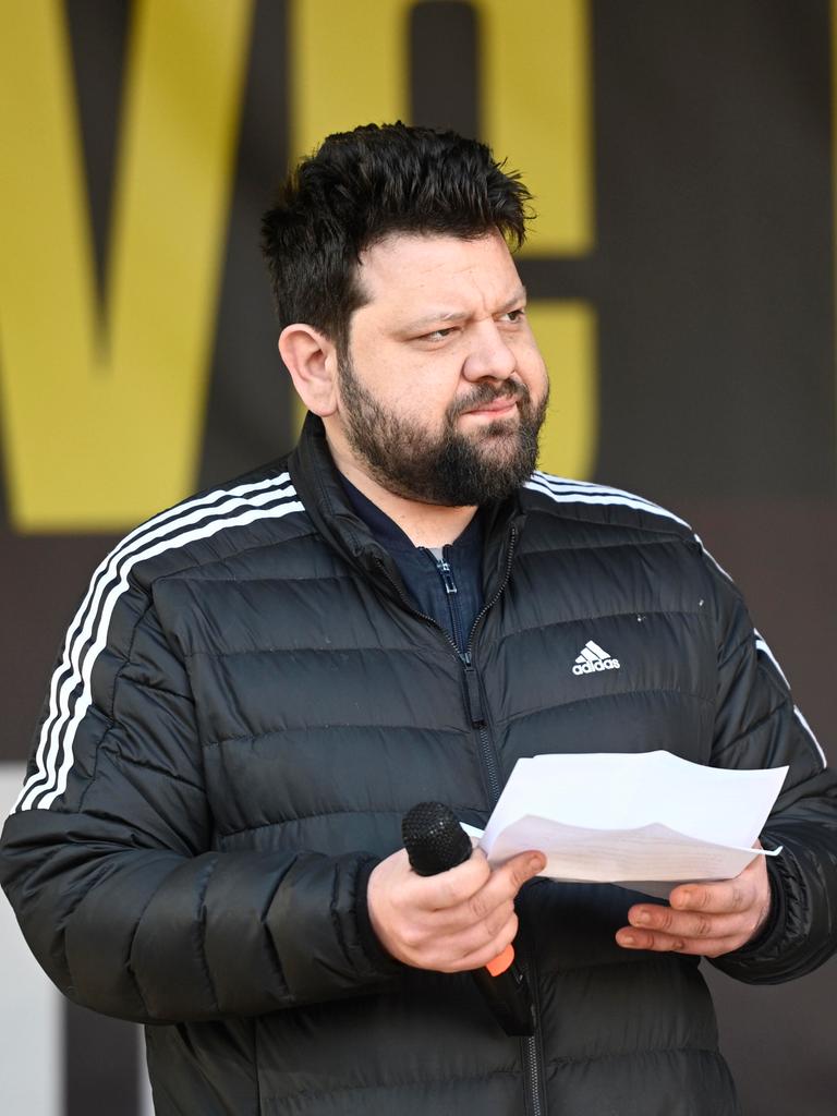 Petar Rosandic spricht auf einer Kundgebung, hält ein Redemanuskript und Mikrofon in den Händen und blickt zur Seite.