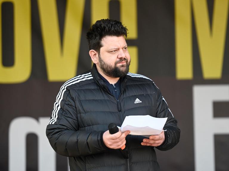 Petar Rosandic spricht auf einer Kundgebung, hält ein Redemanuskript und Mikrofon in den Händen und blickt zur Seite.