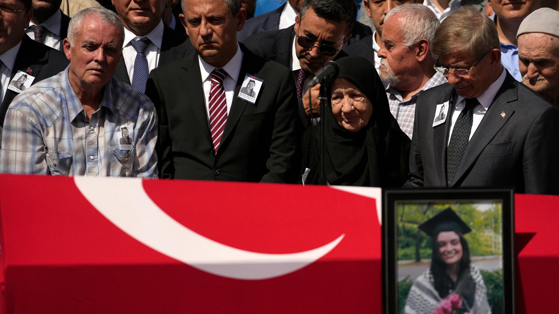 Im Vordergrund ein Sarg, der mit einer türkischen Flagge bedeckt ist, daneben das Bild einer getöteten Frau, im Hintergrund Familienangehörige.