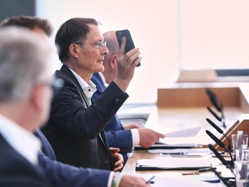 Karl Lauterbach hält bei einer Pressekonferenz sein Handy in die Höhe