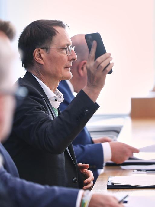 Karl Lauterbach hält bei einer Pressekonferenz sein Handy in die Höhe
