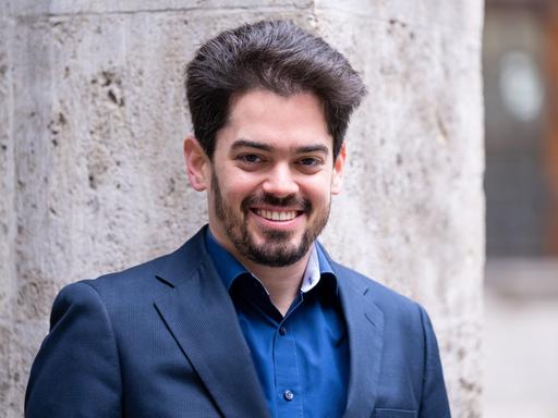Lahav Shani, der zukünftige Chefdirigent der Münchner Philharmoniker, posiert bei seiner Vorstellung in einem blauen Sakko für Pressefotos.