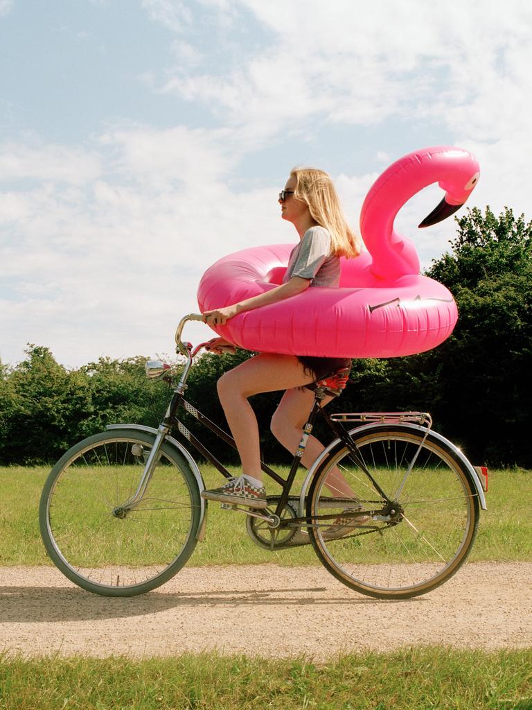 Eine junge Frau auf einem Fahrrad trägt einen aufblasbaren Flamingo um die Hüften.