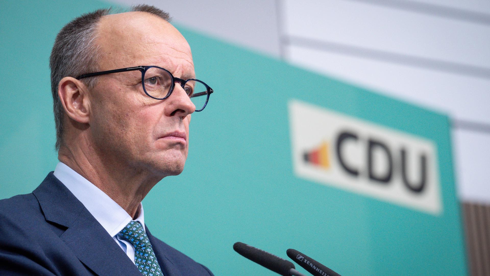 Friedrich Merz steht bei einer Pressekonferenz im Konrad-Adenauer-Haus mit ernstem Blick am Mikrofon vor einem türkisen Hintergrund mit dem Logo der CDU.