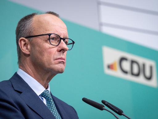 Friedrich Merz steht bei einer Pressekonferenz im Konrad-Adenauer-Haus mit ernstem Blick am Mikrofon vor einem türkisen Hintergrund mit dem Logo der CDU.