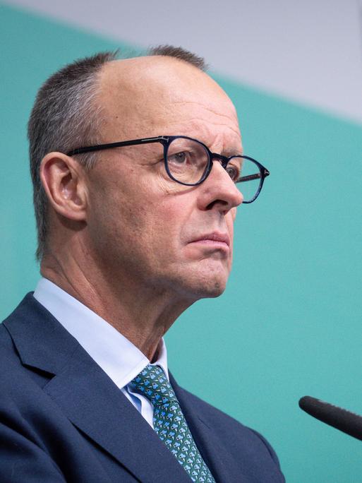 Friedrich Merz steht bei einer Pressekonferenz im Konrad-Adenauer-Haus mit ernstem Blick am Mikrofon vor einem türkisen Hintergrund mit dem Logo der CDU.