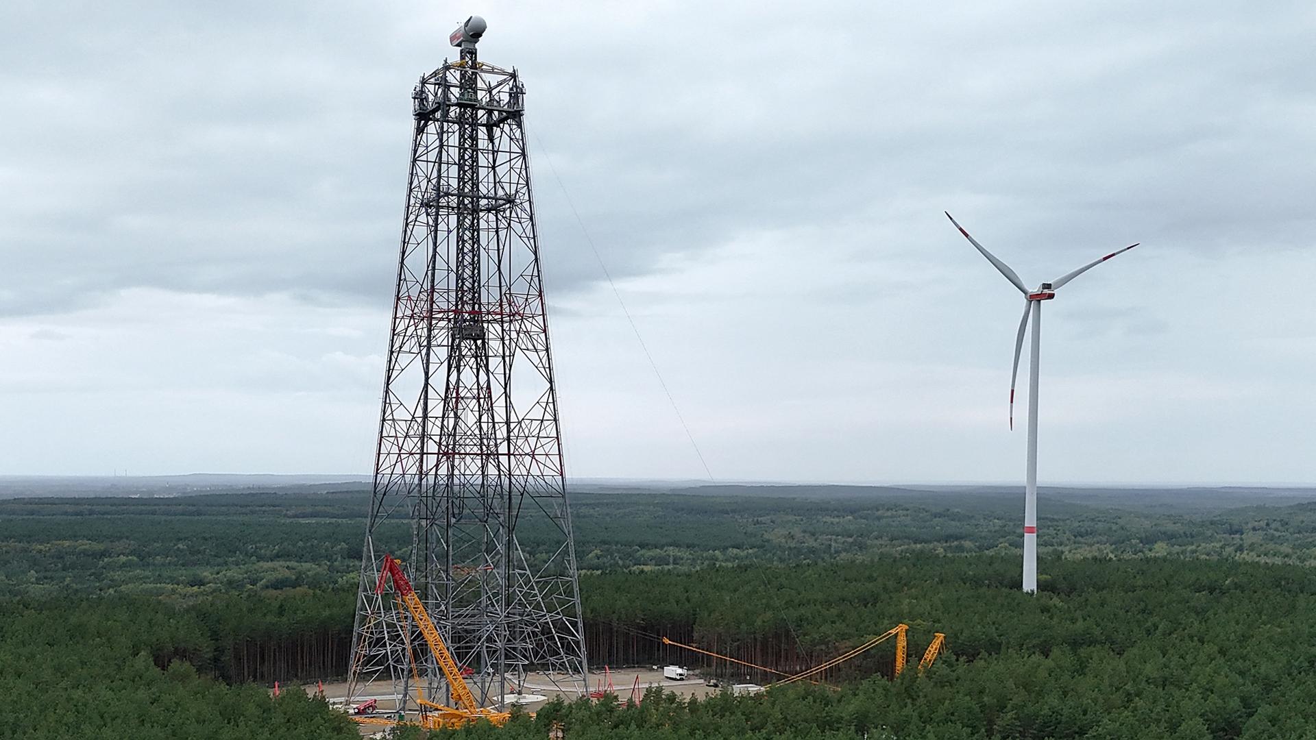 Man sieht den eingerüsteten Höhenwindturm in weiter Landschaft. 