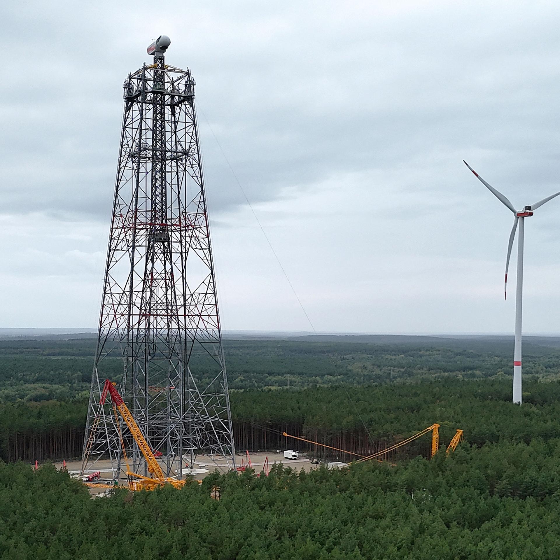 Man sieht den eingerüsteten Höhenwindturm in weiter Landschaft.   