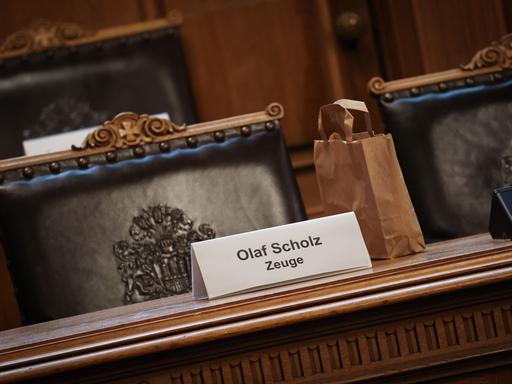 Ein Plastikschild mit dem Text "Olaf Scholz Zeuge" steht auf einem Platz auf der Senatsbank vor Beginn einer Sitzung des Parlamentarischen Untersuchungsausschusses zum Cum-Ex-Komplex