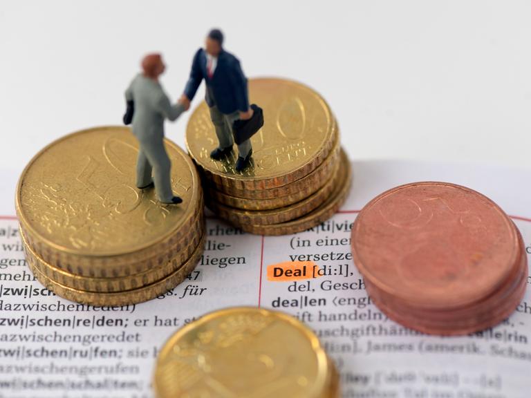 Figuren stehen auf einem Stapel Münzen und geben sich die Hand.