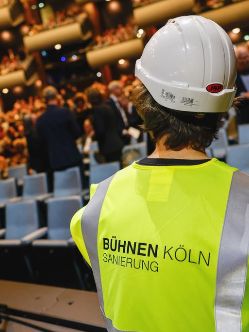 Ein als Bauarbeiter verkleideter Schauspieler sitzt auf der Bühne. Oper und Schauspiel Köln feiern den Wiedereinzug in ihre angestammten Häuser am Offenbachplatz mit einer großen, festlichen Gala. Die Sanierung der Kölner Bühnen hat 14 Jahre gedauert.