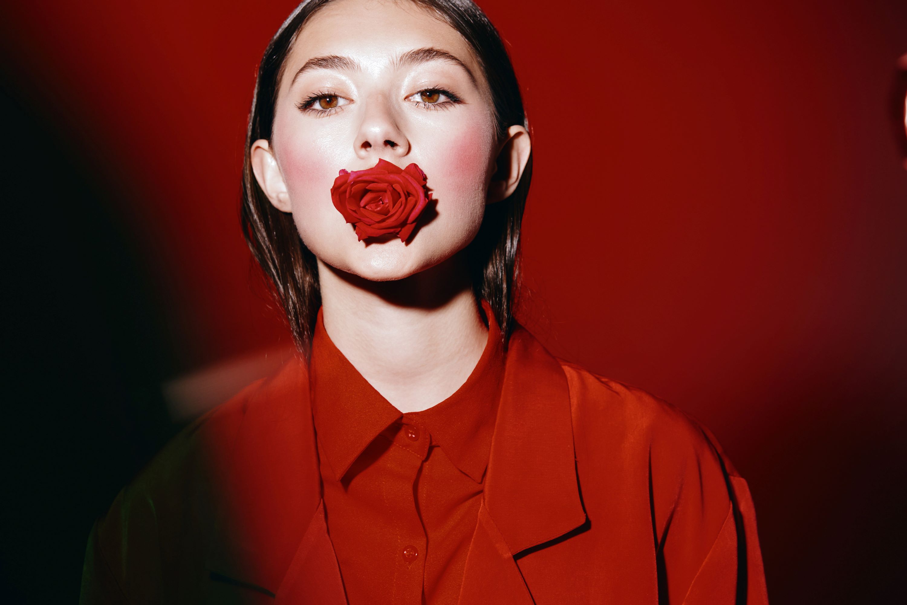 Eine in rot gekleidete Frau mit einer roten Rose im Mund - vor einem roten Hintergrund.