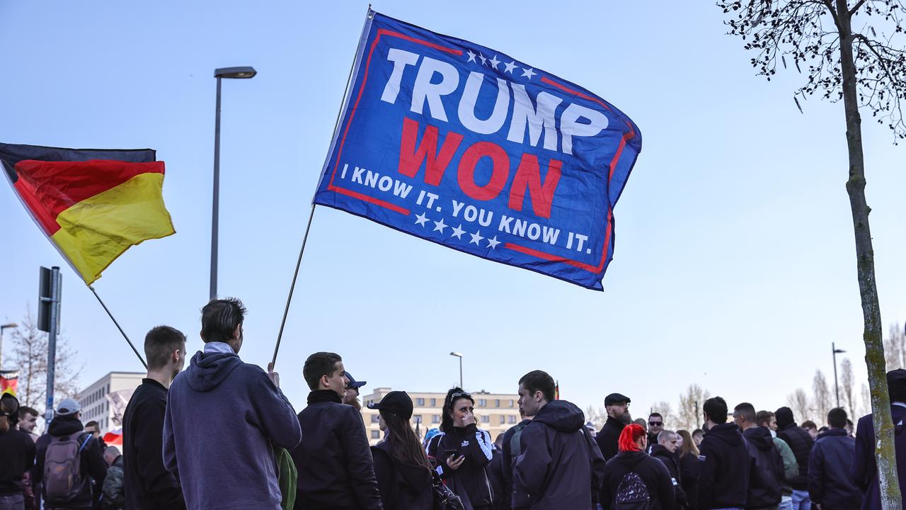 Rechtsextreme Aktivisten der AfD halten ein Transparent zur Unterstützung von US-Präsident Donald Trump hoch, bei einer Demonstration im März 2025 in Berlin, daneben schwingt eine Deutschlandfahne.