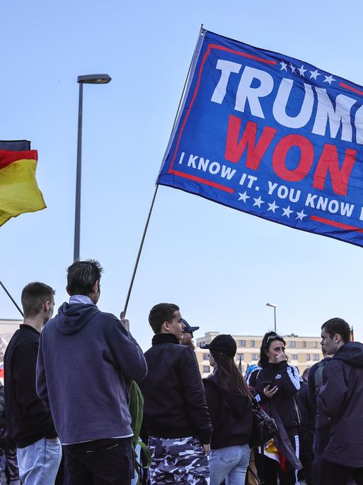 Rechtsextreme Aktivisten der AfD halten ein Transparent zur Unterstützung von US-Präsident Donald Trump hoch, bei einer Demonstration im März 2025 in Berlin, daneben schwingt eine Deutschlandfahne.