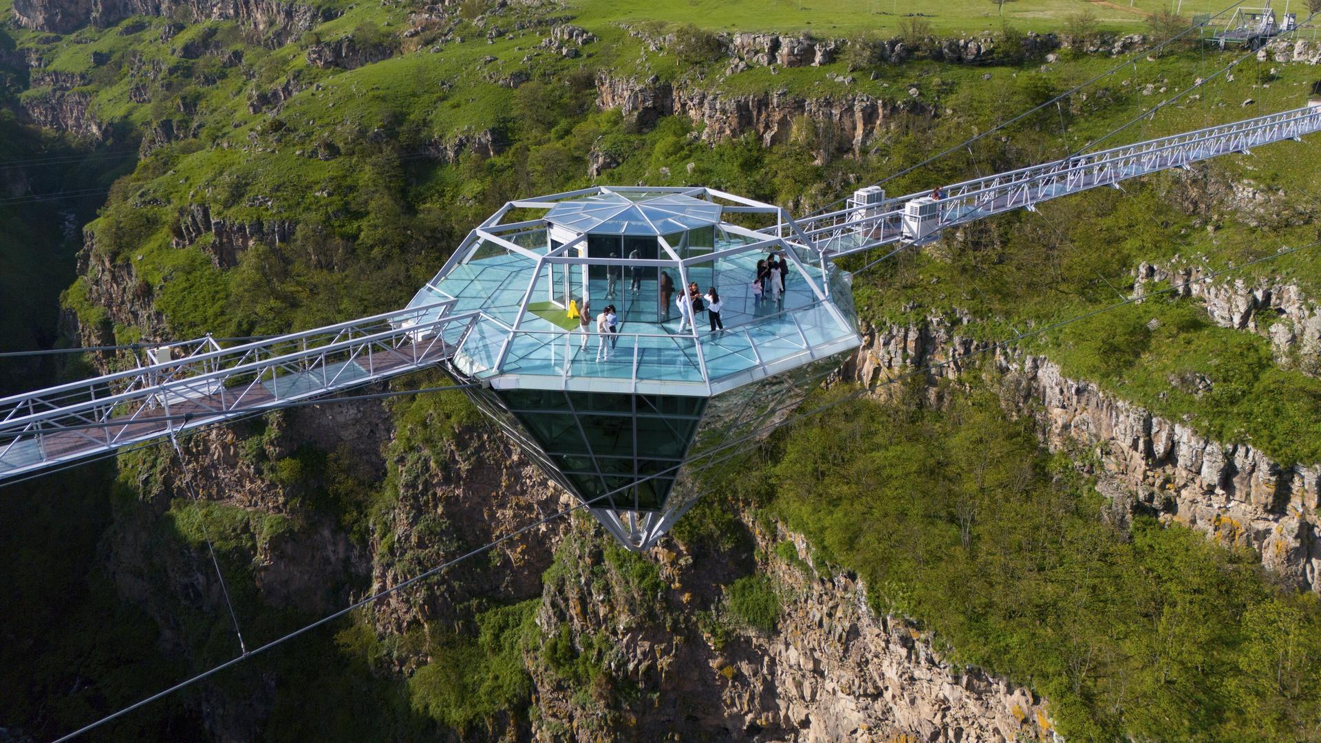 Eine Glasplattform in Diamantform mit Menschen darauf, die eine grüne Schlucht überspannt. Die Diamantenbrücke, in Georgien, die weltweit längste freihängende Konstruktion in einem Naturschutzgebiet.