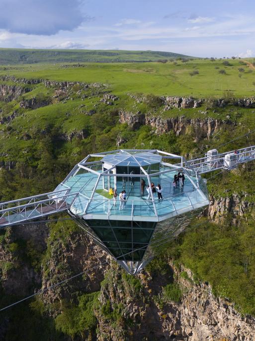 Eine Glasplattform in Diamantform mit Menschen darauf, die eine grüne Schlucht überspannt. Die Diamantenbrücke, in Georgien, die weltweit längste freihängende Konstruktion in einem Naturschutzgebiet.